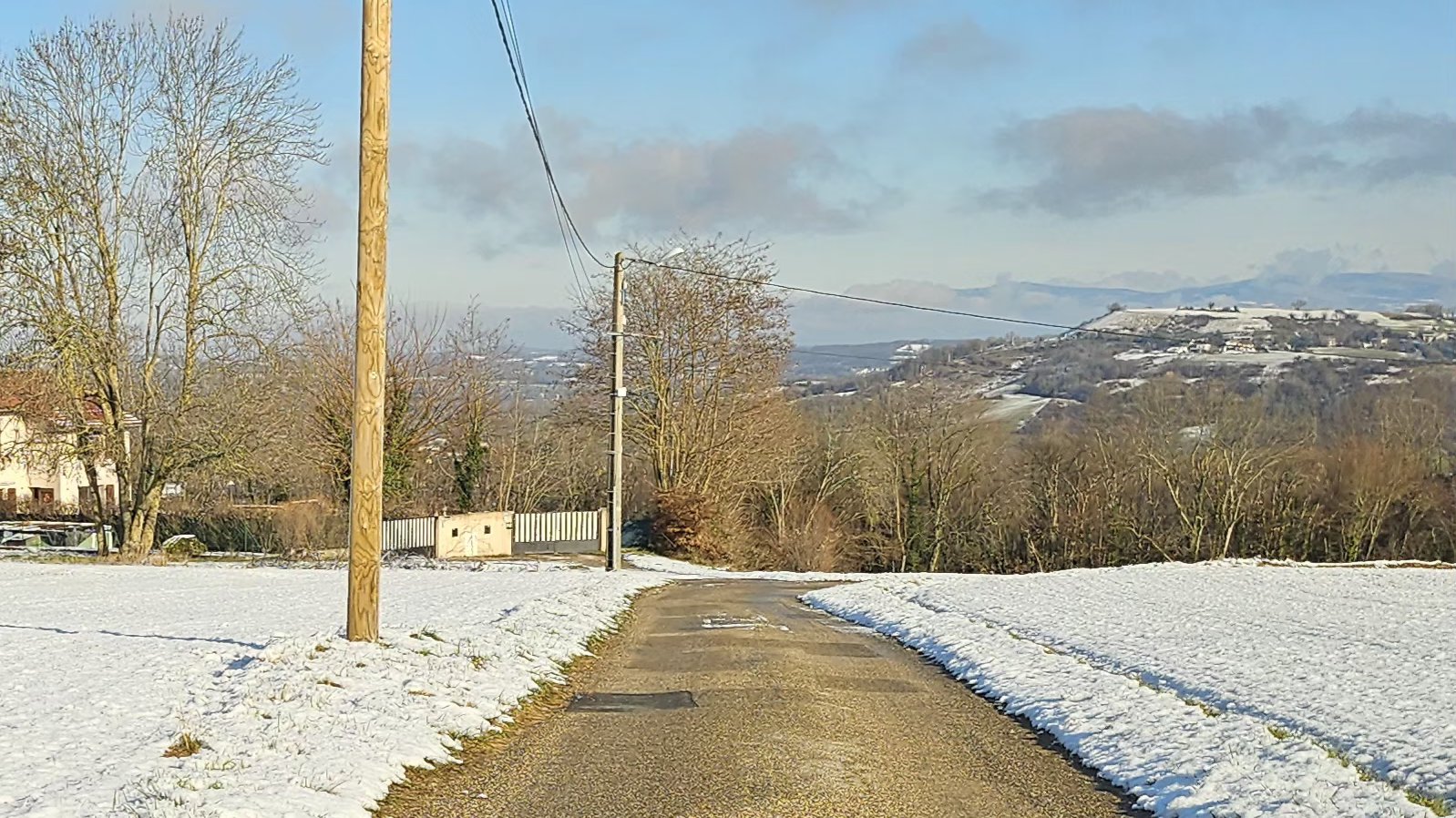 Route rurale dégagée avec neige sur les bas-côtés et panorama sur des collines enneigées — illustration des distances de sécurité par temps froid